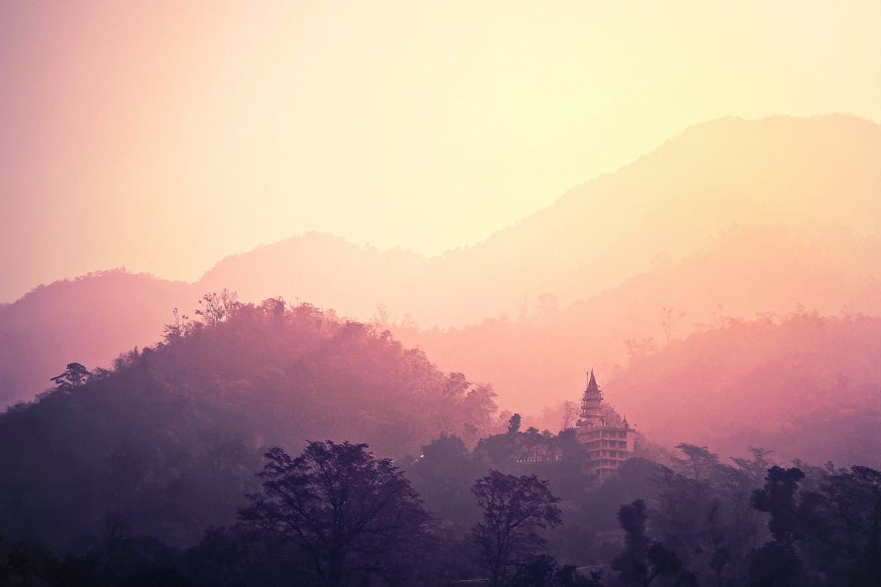 A tranquil view of Rishikesh mountains and temple enveloped in pink hues at sunrise.